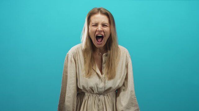 Woman with mouth open screaming, teeth and hands visible, expressive face against turquoise studio backdrop; anger release.