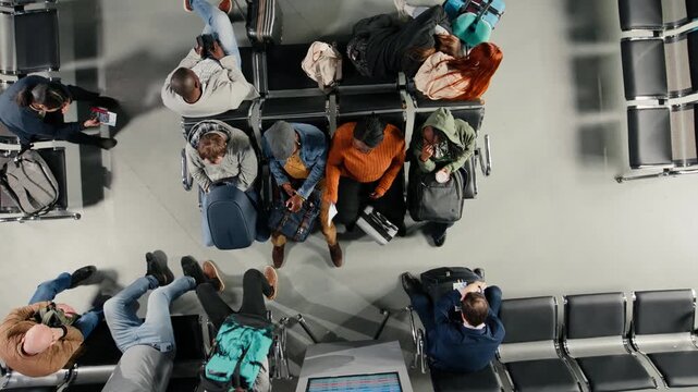 Top down view of furious multiethnic travelers in airport rallied by plane delays shown on departure board. Diverse mad passengers entering frenzy after canceled flights announcement, high angle shot