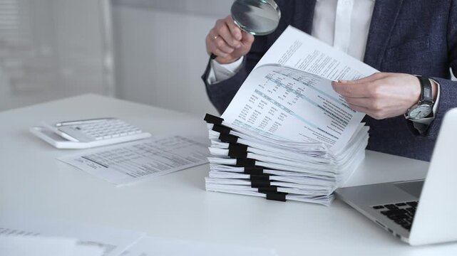 Auditor or accountant inspecting financial documents with a magnifying glass. Analyzing corporate tax records. Legal data. Invoice details. Or business reports. Audit and taxes