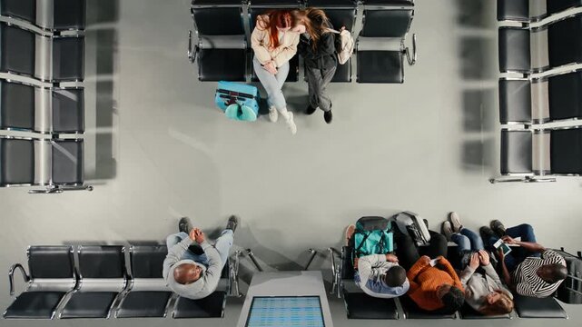 Top down view of travelers rushing through busy airport and people looking at departure board screen. Tourists walking in terminal and people waiting for plane, reading flight timetable