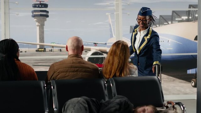 Smiling gate agent talking with tourists in airport, giving flight announcement. Friendly airline personnel inviting people to queue up for boarding gate, concept of organized travel flow