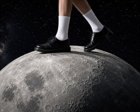 Surreal concept of human feet with black shoes and white socks standing on Earth, creative idea of ​​moonwalking with stars, universe background and space for text.