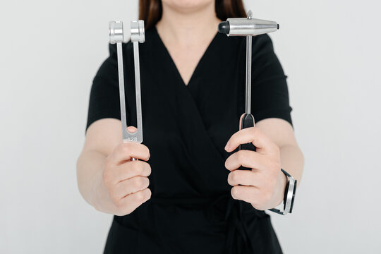young woman doctor, medician in black costume, neurologist holds tuning fork and neurological reflex hammer for testing human reflexes in hands, medical services, tools and equipment for treatment