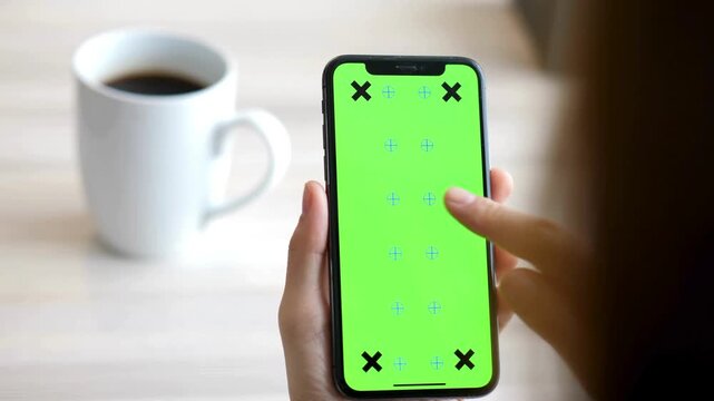 Close up footage of person tapping smartphone with green chroma key screen and tracking markers for motion graphics, app design, and screen replacement editing.
