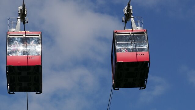 red funicular car leading to the top of the old mountain. The tourist car rides above rocky mountains dotted with cypress trees. Cable car cabins amazing sky and clouds. Cableway, green transportation
