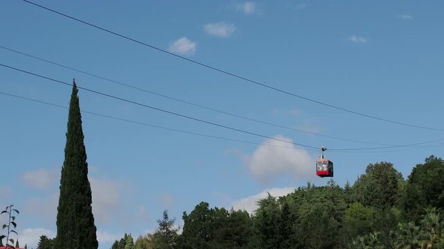 red funicular car leading to the top of the old mountain. The tourist car rides above rocky mountains dotted with cypress trees. Cable car cabins amazing sky and clouds. Cableway, green transportation