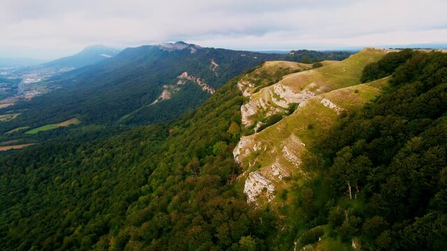 Cinematic drone flight over the mountain spine in Northern Spain. The footage captures a breathtaking perspective of steep rocky cliffs on one side and lush green forests on the other, overlooking a v