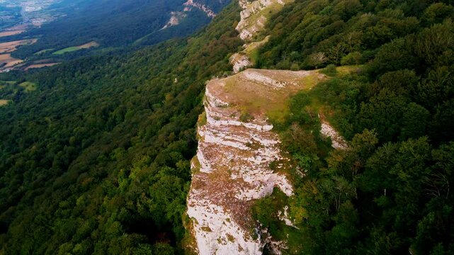 Cinematic drone flight over the mountain spine in Northern Spain. The footage captures a breathtaking perspective of steep rocky cliffs on one side and lush green forests on the other, overlooking a v