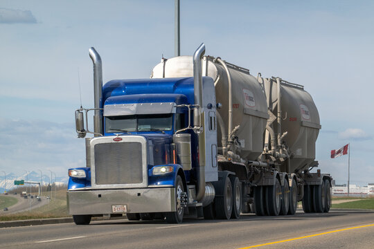 Calgary, AB, Canada. May 8, 2026. A blue Peterbilt semi-truck hauls Trimac bulk trailers along a highway with the Rocky Mountains behind.