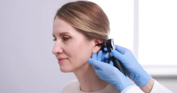 Hearing test. Doctor examining woman's ear with otoscope in clinic, closeup. Camera spinning