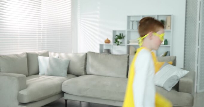 Little boy in superhero costume jumping from sofa at home
