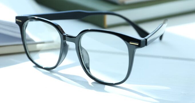 Stylish glasses and books on white wooden table indoors, closeup. Camera moving right
