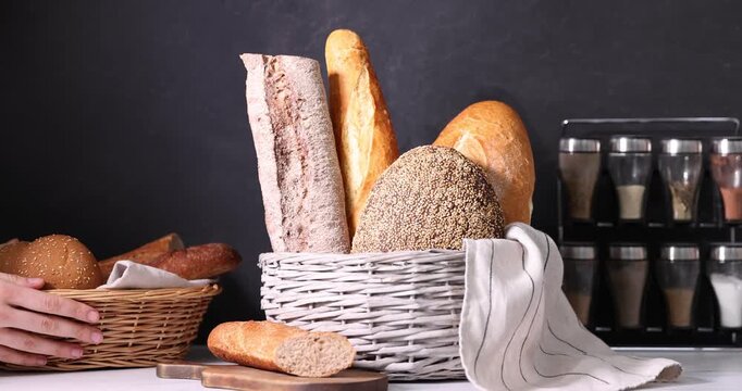 Woman putting wicker basket with different types of fresh bread at white countertop, closeup
