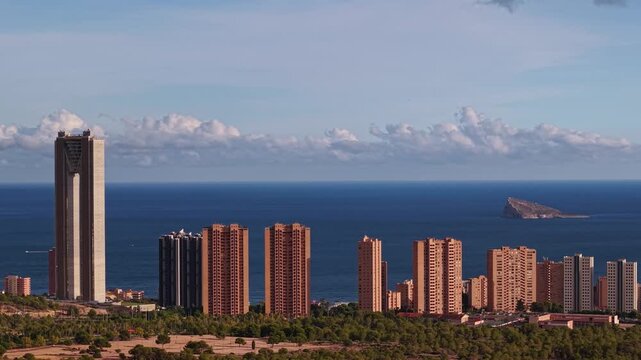 Benidorm cityscape with towering skyscrapers lining mediterranean coastline, capturing benidorm island and dynamic clouds over sparkling blue sea under bright sun, a motion timelapse footage clip.