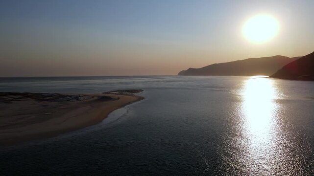 Aerial view of the Sado River and Arrabida mountains at sunset, Troia, Portugal. Drone flying forward towards the setting sun.