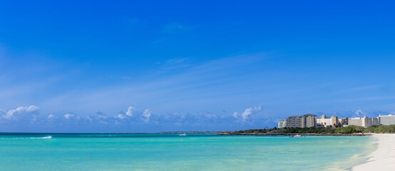Fototapeta premium Panoramic view of Eagle Beach in Aruba featuring turquoise Caribbean water and a white sand coastline with a tropical resort skyline under a clear blue sky