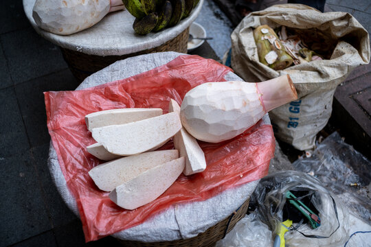 Freshly peeled talas Bogor (Bogor taro) displayed on a woven basket at a traditional market, with sliced taro pieces, peels, and local produce visible in the background.