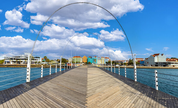View from the wooden deck of the Queen Emma Bridge towards the iconic colorful colonial architecture of the Punda district in Willemstad, Curacao under a blue sky with clouds in Caribbean