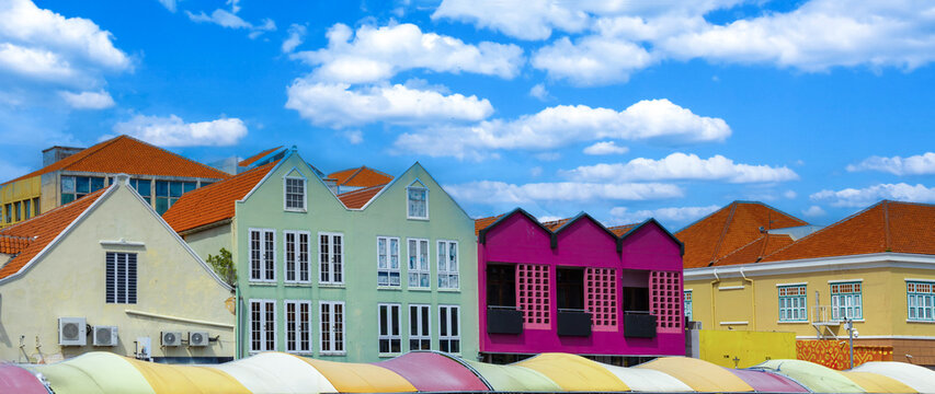 Traditional boats at the floating market in front of vibrant colonial architecture in the Punda district of Willemstad Curacao under a blue cloudy sky