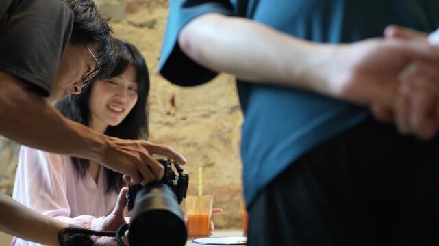Camera captures joyful moments during candid video shoot. Two women laugh, sipping drinks, engaged in conversation. Third person guides the photographer with expressive gestures