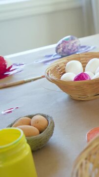 Vertical video: Panning camera revealing open yellow paint jar on craft table, showing painted eggs