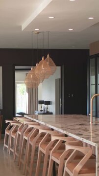Vertical video: Starting pan, camera moving across marble island showing stools lights faucet plant