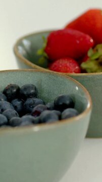 Vertical video: Tilting camera right, showing teal bowls in kitchen, focusing berries with drops