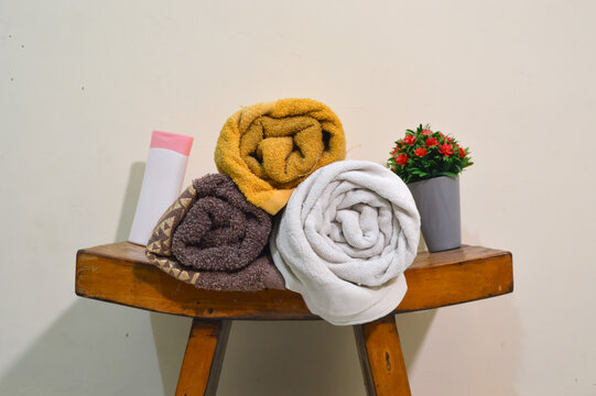 A centered middle height shot of neatly rolled white and blue towels on a curved wooden table with a bottle of body lotion and a small artificial lavender plant in the background.