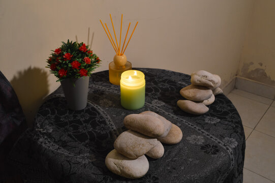 A high perspective from the quarter left angle capturing a burning candle and zen stones placed on a textured green cloth for a home wellness setup.