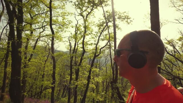 High-quality 4k b-roll footage of an active mature man (50+) with a backpack and headphones running, hiking, and walking on a forest trail. Concept of healthy aging, active lifestyle.