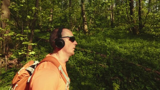High-quality 4k b-roll footage of an active mature man (50+) with a backpack and headphones running, hiking, and walking on a forest trail. Concept of healthy aging, active lifestyle.