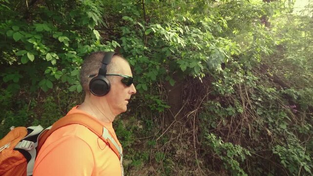 High-quality 4k b-roll footage of an active mature man (50+) with a backpack and headphones running, hiking, and walking on a forest trail. Concept of healthy aging, active lifestyle.