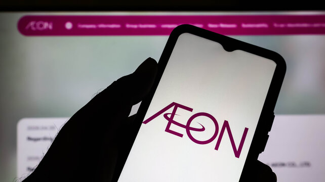 Closeup of a hand holding a smartphone displaying the aeon logo with a blurred website background in the dark