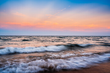 Obraz premium sunset over ocean with waves crashing on beach