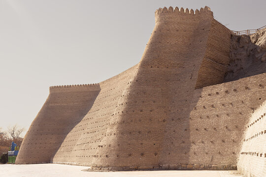 Ark Fortress walls in Bukhara with massive undulating brick buttresses and crenellated parapets. Ideal for travel publications, heritage content, and architectural features about Central Asia.