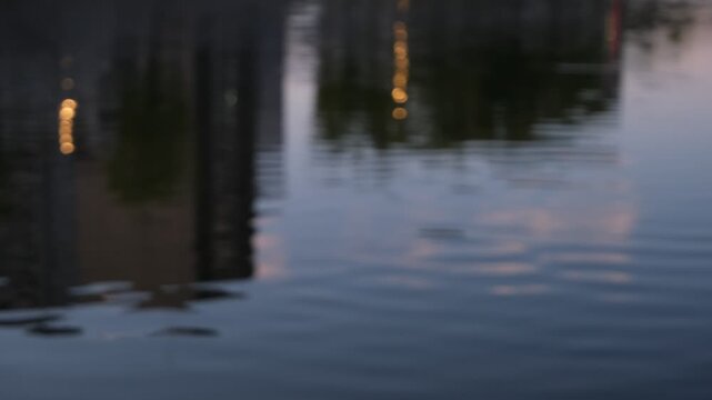 Evening building and street light reflections rippling on flowing river water, silent abstract footage