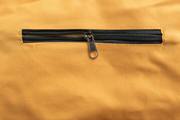 Close-up of a black zipper on yellow canvas fabric texture background. © Renhue