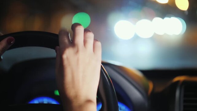 Close up shot of a person's hands steering a car at night with blurry city lights in background, driver navigating traffic on road footage.