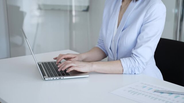 Businesswoman's hands typing on a laptop, performing data entry, communicating via email, or engaging in a productive online task at an office desk, highlighting focus and efficiency
