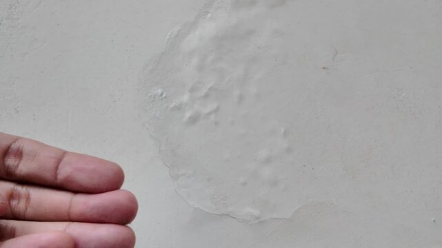 Close up of a large, circular paint blister caused by water trapped behind the paint film on a residential wall.