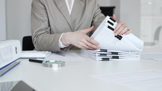 Businesswoman hands organizing stack of papers with binder clips, working on financial documents and official reports in office. Audit and taxes concept