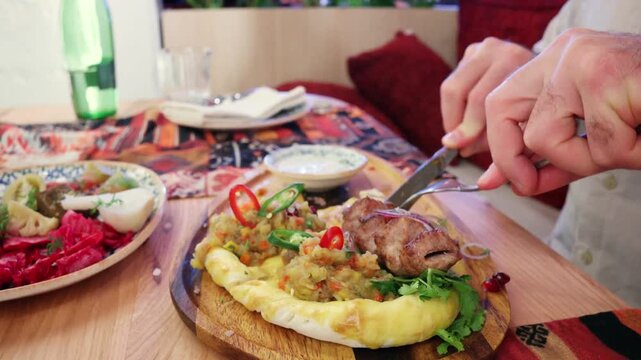 Person cuts delicious meat dish with vegetables and herbs on flatbread at table.