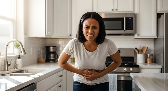 Woman in kitchen clutching stomach due to severe hunger or pain