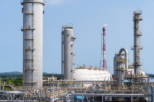 Wide view of large distillation columns, storage tanks, and a flare stack at an operating gas plant under a clear blue sky.