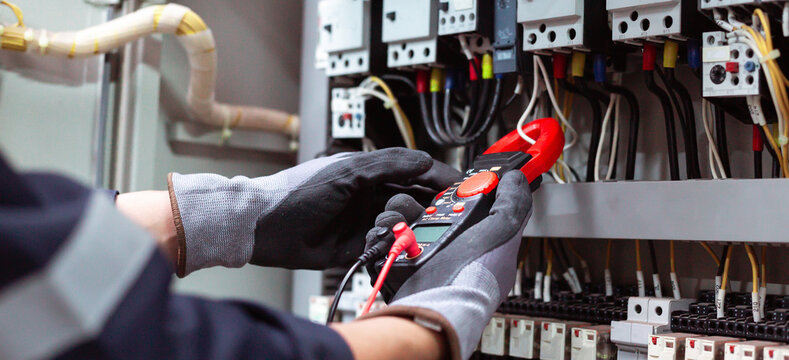 Close-up of technician measuring amperage with clamp multimeter in industrial electric cabinet.