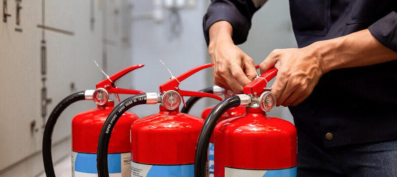 Professional technician checking and inspecting pressure gauge of red fire extinguishers for annual safety maintenance and compliance in industrial building.