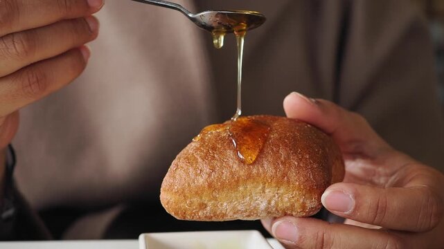 Honey is poured on a fresh baked bread roll