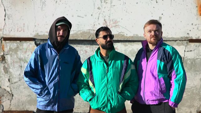 Trio Of Men Dressed In Retro Attire Standing Confidently With Gritty Urban Environment Behind Them. Media
