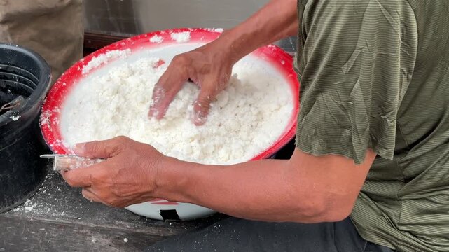 A traditional food vendor mixes the traditional Putu cake batter, stirring it until it has a grainy texture like wet sand.
