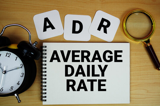 ADR Average Daily Rate text written on notepad with magnifying glass and alarm clock on wooden background